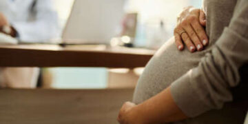 Una persona embarazada consulta con un médico en un escritorio, de cerca en manos del vientre.