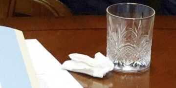 Imagen de un pañuelo, papeles y un vaso en una mesa.