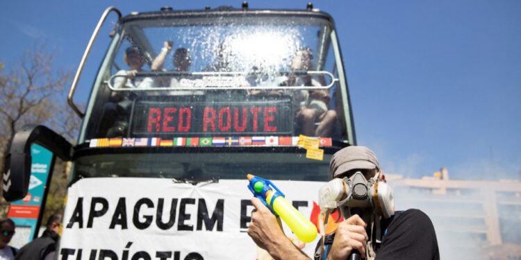 Los manifestantes que bloquean un autobús turístico con un banner leyendo "Vamos a apagar el fuego turístico".