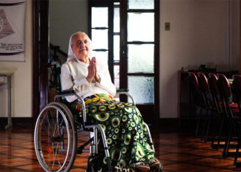 Mujer anciana en una silla de ruedas, rezando.