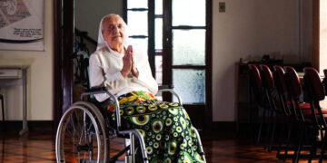 Mujer anciana en una silla de ruedas, rezando.