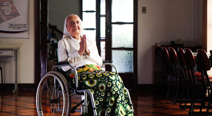 Mujer anciana en una silla de ruedas, rezando.