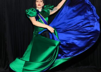 Lady Gaga con un vestido de satén verde y azul detrás del escenario.
