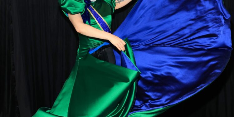 Lady Gaga con un vestido de satén verde y azul detrás del escenario.
