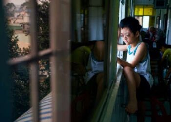 Un niño pequeño con discapacidades del Agente Orange mira afuera mientras se sienta en un alféizar