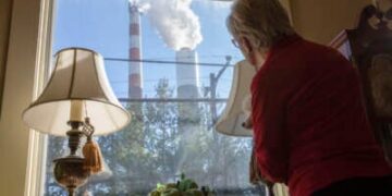 Marti Blake mira por su ventana delantera en la chimenea de la planta de energía a carbón de Cheswick en Springdale, Pensilvania, el 27 de octubre de 2017. Blake dice que la cantidad de dióxido de azufre, óxido de nitrógeno y partículas de carbón que se originan en la planta ha impactado su salud, así como las de la zona circundante.