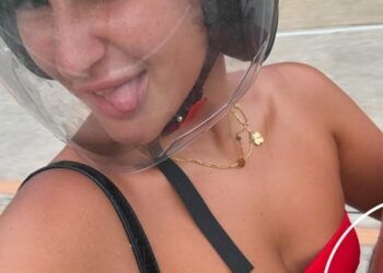 Mujer que usa un casco de motocicleta y una tapa del bikini rojo sobresaliendo de su lengua.