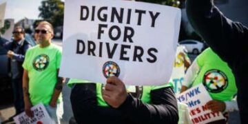Una persona con una camisa verde sostiene un letrero que lee "Dignidad para conductores" con el logotipo de los conductores de viaje compartido debajo del texto