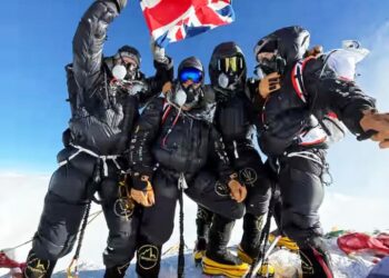 Cuatro escaladores británicos en el Monte Everest Summit, sosteniendo una bandera del Reino Unido.