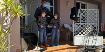 Un hombre enmascarado se encuentra con dos niños enmascarados en un porche, rodeado de desorden.