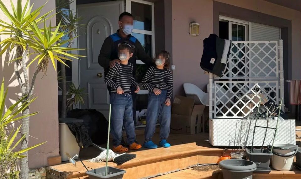 Un hombre enmascarado se encuentra con dos niños enmascarados en un porche, rodeado de desorden.