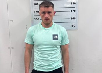 Mugshot de un hombre con una camisa verde menta y pantalones cortos negros.