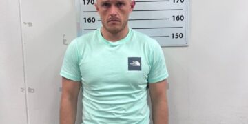 Mugshot de un hombre con una camisa verde menta y pantalones cortos negros.