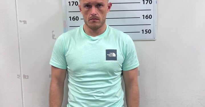 Mugshot de un hombre con una camisa verde menta y pantalones cortos negros.