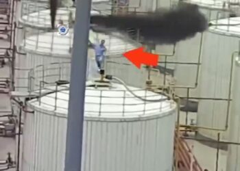 Trabajador en plataforma cerca de la pluma de humo industrial.
