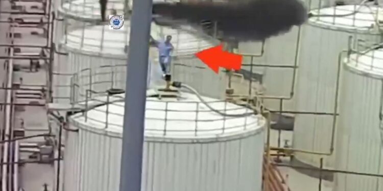 Trabajador en plataforma cerca de la pluma de humo industrial.