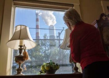 Marti Blake mira por su ventana delantera en la chimenea de la planta de energía a carbón de Cheswick en Springdale, Pensilvania, el 27 de octubre de 2017. Blake dice que la cantidad de dióxido de azufre, óxido de nitrógeno y partículas de carbón que se originan en la planta ha impactado su salud, así como las de la zona circundante.