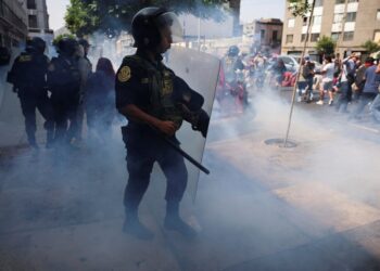 Oficial de policía que usa un escudo antidisturbios para dispersar a los manifestantes con gases lacrimógenos.
