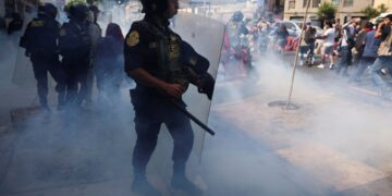 Oficial de policía que usa un escudo antidisturbios para dispersar a los manifestantes con gases lacrimógenos.