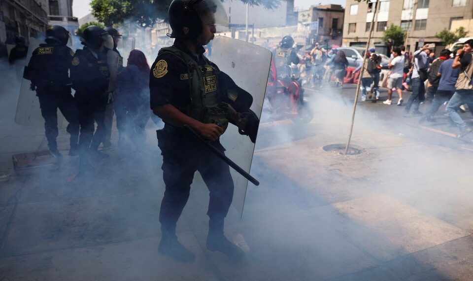 Oficial de policía que usa un escudo antidisturbios para dispersar a los manifestantes con gases lacrimógenos.