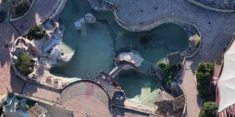 Vista aérea de un parque marino abandonado con dos orcas y doce delfines.