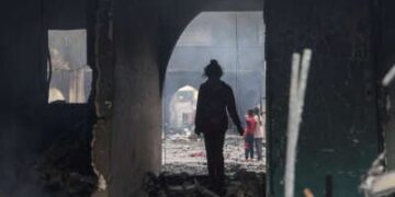 Una niña se encuentra siluada en un arco parcialmente destruido que conduce a una escuela destruida