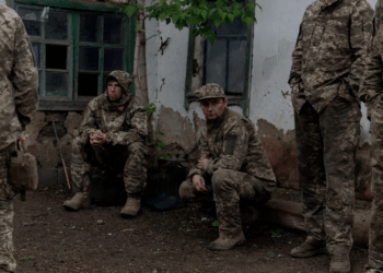Soldados en camuflaje descansando cerca de un edificio.