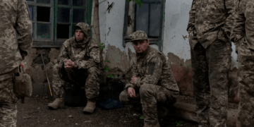 Soldados en camuflaje descansando cerca de un edificio.
