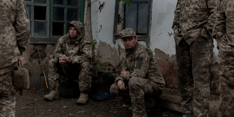 Soldados en camuflaje descansando cerca de un edificio.