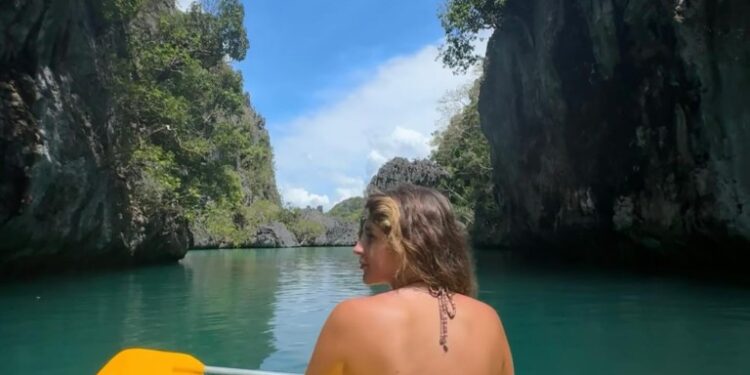 Mujer kayaking a través de un canal estrecho entre los acantilados de piedra caliza.