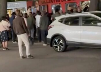 Captura de pantalla de una multitud de personas se reunió alrededor de un autobús y un SUV blanco.
