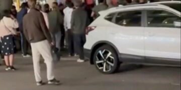 Captura de pantalla de una multitud de personas se reunió alrededor de un autobús y un SUV blanco.