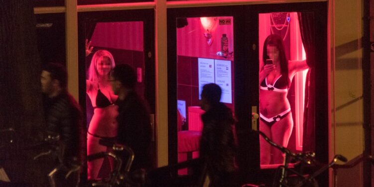 Las trabajadoras sexuales se ven detrás de las ventanas en el Distrito de Luz Roja en Amsterdam, Países Bajos, 24 de abril de 2015. El distrito de luz roja de la ciudad se encuentra en una red de callejones que contienen aproximadamente trescientas cabañas de una habitación alquiladas por prostitutas que ofrecen sus servicios sexuales desde detrás de una ventana o puerta de vidrio, típicamente iluminadas con luces rojas. Amsterdam es uno de los destinos turísticos  populares de Europa, que recibe  de 4.63 millones de visitantes internacionales anualmente. (Foto de Horacio Villalobos/Corbis a través de Getty Images)