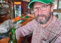 Un hombre con una gorra verde Heineken se encuentra en un bar con una cerveza Heineken.