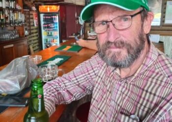 Un hombre con una gorra verde Heineken se encuentra en un bar con una cerveza Heineken.