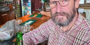 Un hombre con una gorra verde Heineken se encuentra en un bar con una cerveza Heineken.