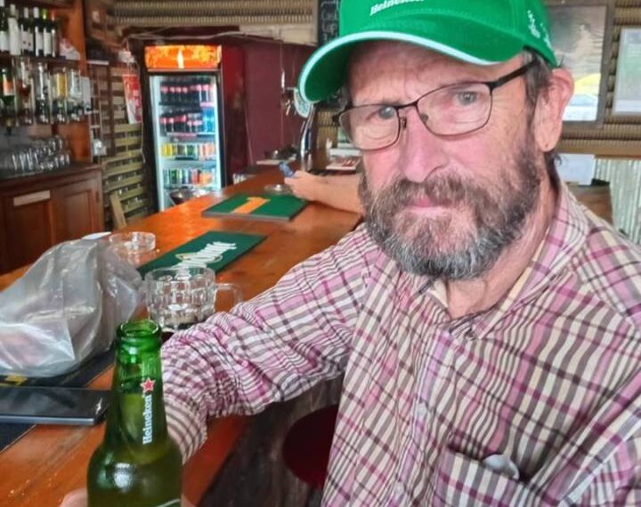 Un hombre con una gorra verde Heineken se encuentra en un bar con una cerveza Heineken.