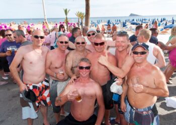 Grupo de hombres británicos sin camisa bebiendo en una playa en Benidorm.