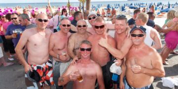 Grupo de hombres británicos sin camisa bebiendo en una playa en Benidorm.