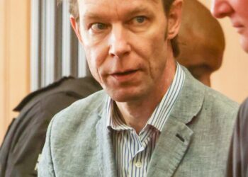 Un hombre con traje y camisa a rayas mira la cámara