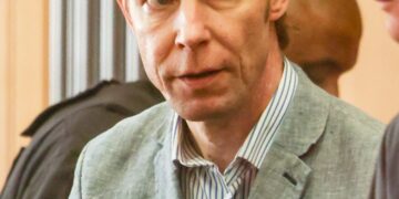 Un hombre con traje y camisa a rayas mira la cámara