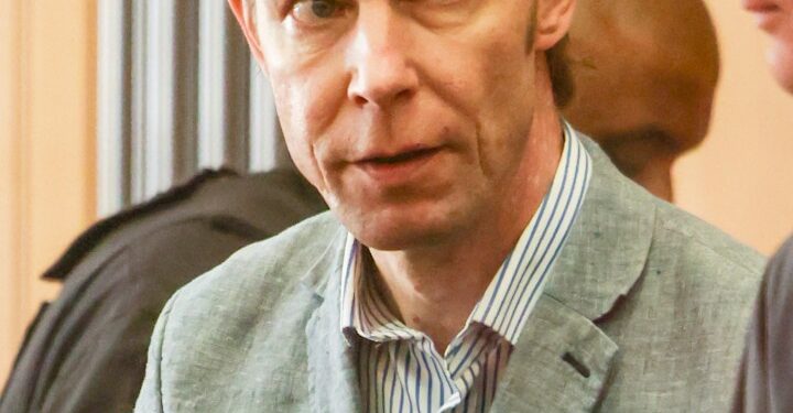 Un hombre con traje y camisa a rayas mira la cámara