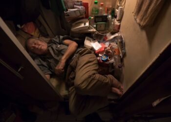 Anciano durmiendo en una pequeña habitación desordenada.