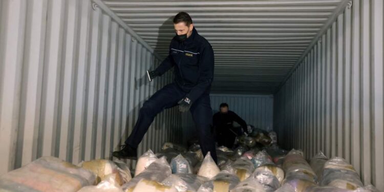 Funcionarios de aduanas que inspeccionan un contenedor de envío lleno de paquetes de cocaína incautada.
