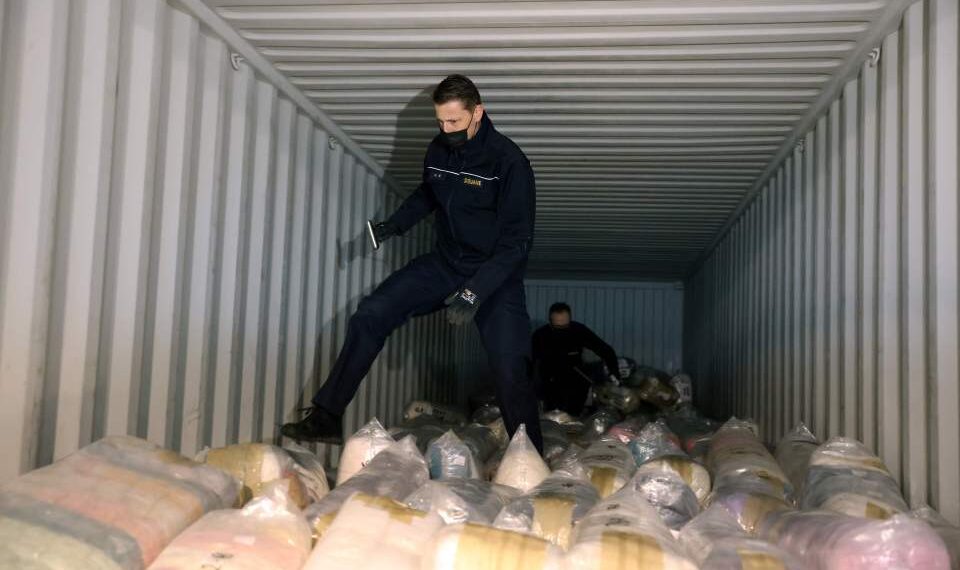 Funcionarios de aduanas que inspeccionan un contenedor de envío lleno de paquetes de cocaína incautada.