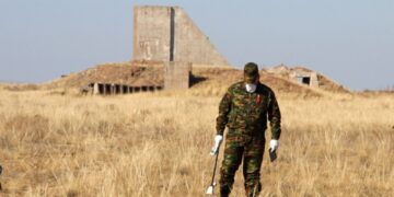 Un hombre con ropa de camuflaje mide los niveles de radiación cerca de los restos de una estructura.