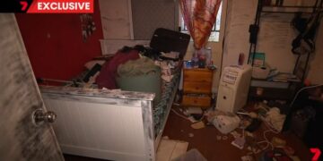 Dormitorio desordenado con pertenencias esparcidas por el piso y la cama.