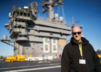 Hombre con gafas de sol de pie en la cubierta de un portaaviones.