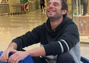 Un hombre sonriente sentado en un coche de parachoques azul en un centro comercial.