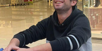 Un hombre sonriente sentado en un coche de parachoques azul en un centro comercial.